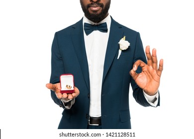 cropped view of african american man holding box with wedding ring and showing ok sign isolated on white 