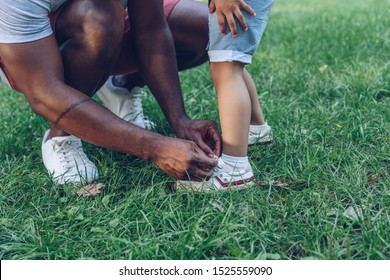 cropped view of african american man tying shoelaces of son in park