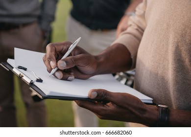 Cropped View Of African American Man Writing Something On Paper In Clipboard