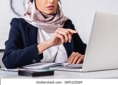 Cropped View Of Arabian Interpreter Pointing With Finger Near Laptop And Digital Translator On Blurred Foreground