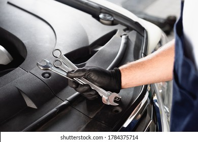 Cropped View Of Auto Mechanic In Latex Glove Holding Wrenches Near Open Hood