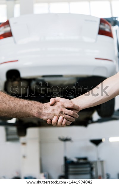 cropped view of auto mechanic shaking hands with man in\
garage 