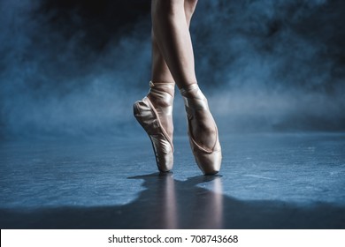 cropped view of ballet dancer in pointe shoes in dark studio with smoke