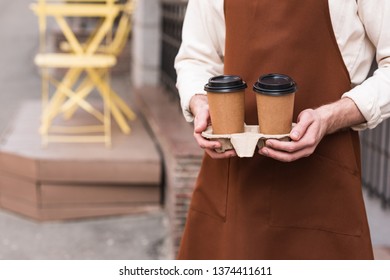 Cropped View Of Barista In Brown Apron Holding Take-out Cup Carrier With Coffee