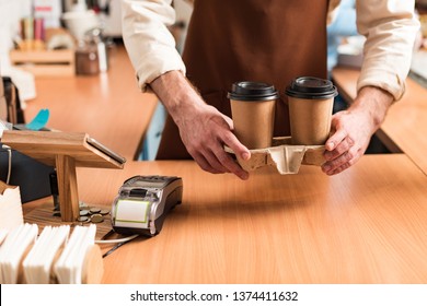 Cropped View Of Barista In Brown Apron Holding Take-out Cup Carrier With Coffee