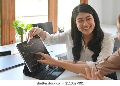 Cropped view beautiful and smiley Asian woman explaining graphs on tablet to colleague in the office. - Shutterstock ID 2113027301