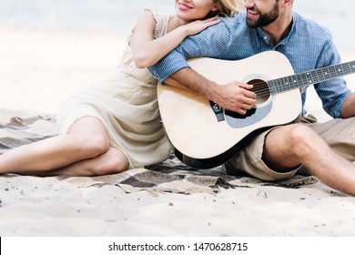 cropped view of beautiful young couple sitting on blanket with acoustic guitar at beach near sea - Powered by Shutterstock