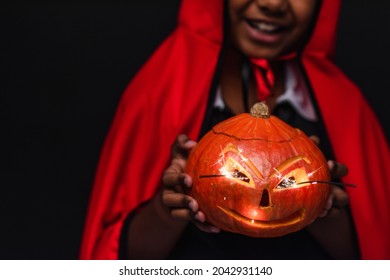 Cropped View Of Blurred And Happy African American Boy In Devil Halloween Costume Holding Carved Pumpkin Isolated On Black