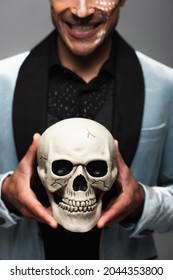 Cropped View Of Blurred Man With Sarcastic Smile Holding Creepy Skull Isolated On Grey