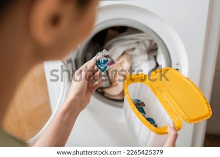 Cropped view of blurred woman holding washing capsule and box near machine in laundry room