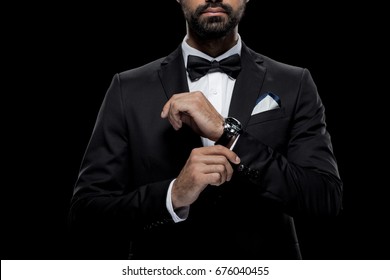 cropped view of businessman in bow tie and tuxedo with watch, isolated on black 