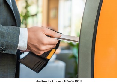 Cropped view of businessman holding wallet and credit card, while standing near atm on blurred background - Shutterstock ID 1856521918