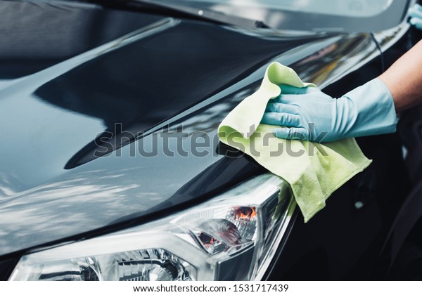 cropped\
view of car cleaner wiping black car with\
rag