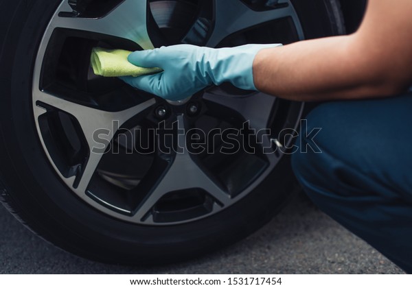 cropped\
view of car cleaner wiping car wheel with\
rag