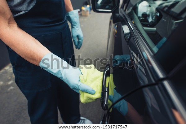 cropped view of car cleaner wiping handle of car door\
with rag