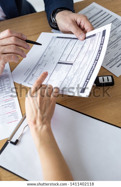 Cropped view of car dealer showing car loan\
application form to woman in\
office