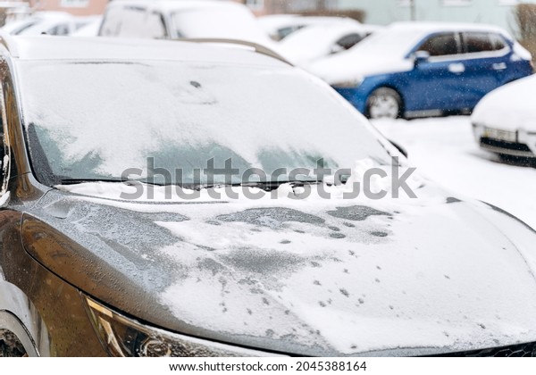 Cropped view of the car hood under the snow after\
a snowfall. Cars in the snow-covered parking lot. Snowy winter and\
lots of snow concept