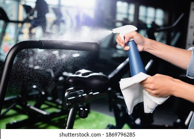 Cropped View Of Charwoman Spraying Detergent While Cleaning Exercising Machine In Gym