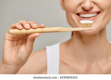 cropped view of cheerful woman holding toothbrush with toothpaste and smiling at camera on grey - Powered by Shutterstock