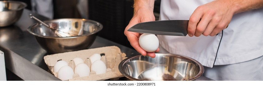 Cropped View Of Chef In Uniform Holding Knife Near Raw Egg Above Bowl While Cooking In Kitchen, Banner