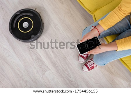 Cropped view of child with smartphone on sofa near robotic vacuum cleaner on floor in living room Stock photo © 