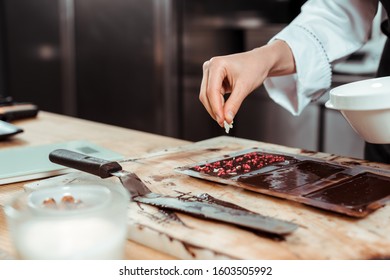 cropped view of chocolatier adding coconut flakes on dark chocolate bar
