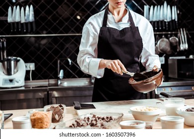 cropped view of chocolatier in apron holding silicone spatula while mixing chocolate in bowl