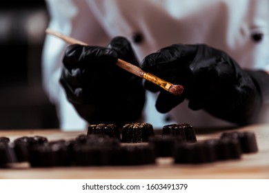 cropped view of chocolatier holding brush near chocolate candies