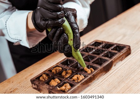 cropped view of chocolatier holding pastry bag with caramelized nuts near chocolate molds