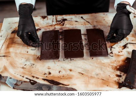 cropped view of chocolatier in latex gloves near chocolate bars