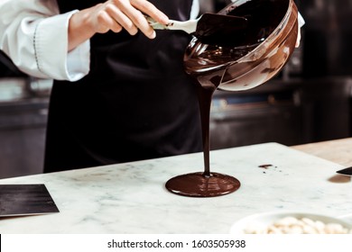 cropped view of chocolatier pouring melted chocolate on marble surface