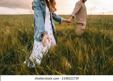 cropped view of couple holding hands and walking on green summer meadow