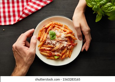 cropped view of couple holding plate with tasty bolognese pasta on black wooden table with basil, cutlery and check napkin