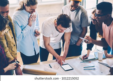 Cropped view of creative students solving training problems of planning while standing at desktop with sketches and blueprints in university interior.Hipster guys collaborating on new building project - Shutterstock ID 1012215052