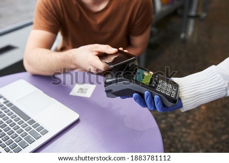 Cropped view of the customer making wireless or contactless payment using smartphone. Store worker accepting payment over nfc technology