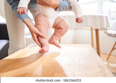 Cropped view of the cute boy taking first steps while his caucasian young mother holding his legs. Baby growth and development concept