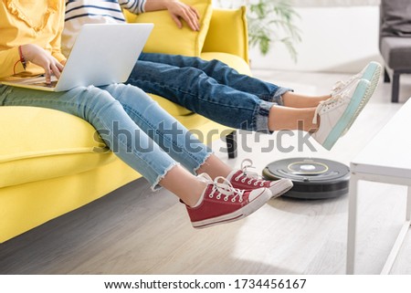Cropped view of daughter with laptop near mother with raised legs on sofa and robotic vacuum cleaner on floor in living room Stock photo © 