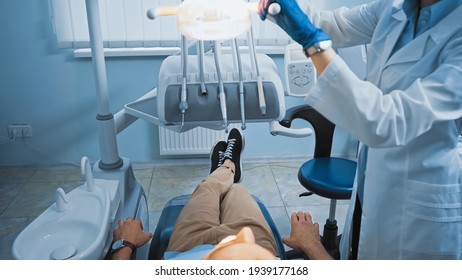 Cropped View Of Dentist Adjusting Lamp Above Patient Sitting In Medical Chair