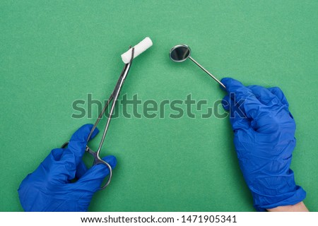 cropped view of dentist in blue latex gloves holding scissors with cotton pad and medical mirror on green 