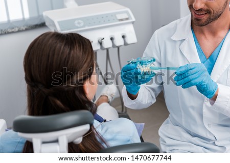 cropped view of dentist in latex gloves holding toothbrush near teeth model and girl