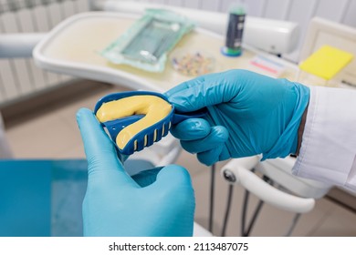 Cropped view of the dentist wearing protective gloves squeezes out the mass into the articulator with teeth mould. - Shutterstock ID 2113487075