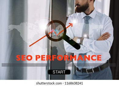 cropped view of developer with crossed arms standing near window with SEO performance and search sign