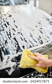 cropped view of devoted hard working serviceman in uniform washing black modern car with sponge
