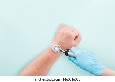cropped view of doctor examining hand of man with dermatoscope isolated on blue