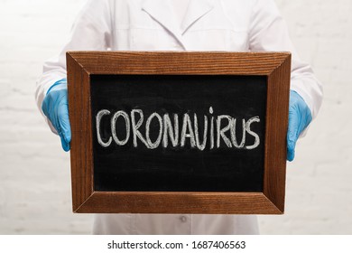 Cropped view of doctor holding blackboard with coronavirus lettering on white background - Shutterstock ID 1687406563