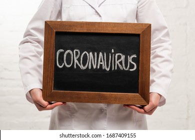 Cropped view of doctor holding chalkboard with coronavirus lettering on white background - Shutterstock ID 1687409155