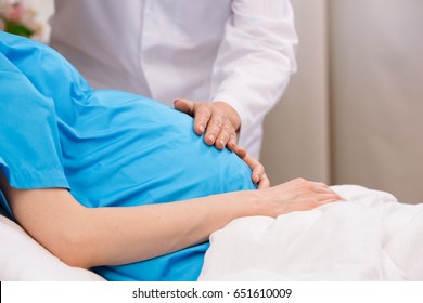 cropped view of doctor touching belly of pregnant woman lying in clinic