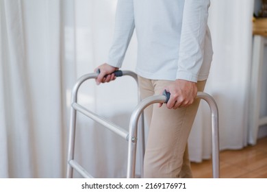 Cropped View Of Elderly Man Walking With Frame At Home, Closeup. Young Male Asian Using Medical Equipment To Move Around His House. Disabled Older Person In Need Of Professional Help