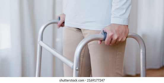 Cropped View Of Elderly Man Walking With Frame At Home, Closeup. Young Male Asian Using Medical Equipment To Move Around His House. Disabled Older Person In Need Of Professional Help