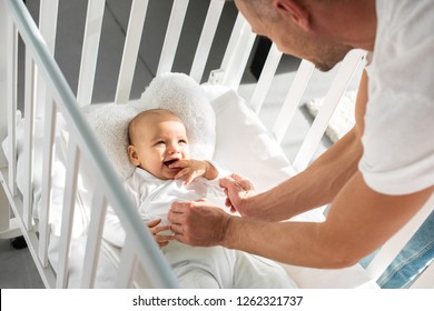 Cropped View Of Father Putting Infant Daughter Into Baby Crib 